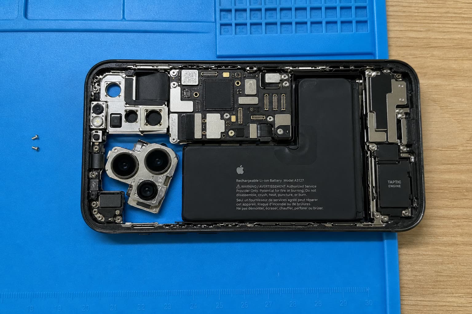 Opened iPhone 15 Pro Max on the repair mat, with the battery, cameras, and board visible