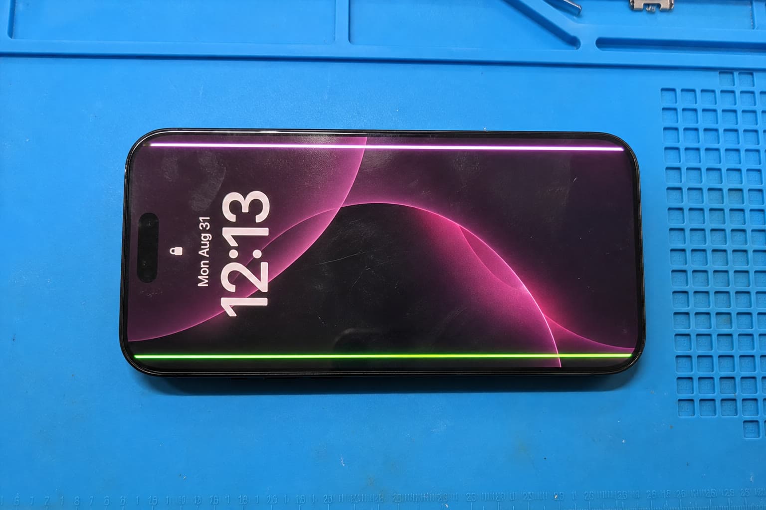 iPhone 16 Pro on the repair mat with green and white lines across the display