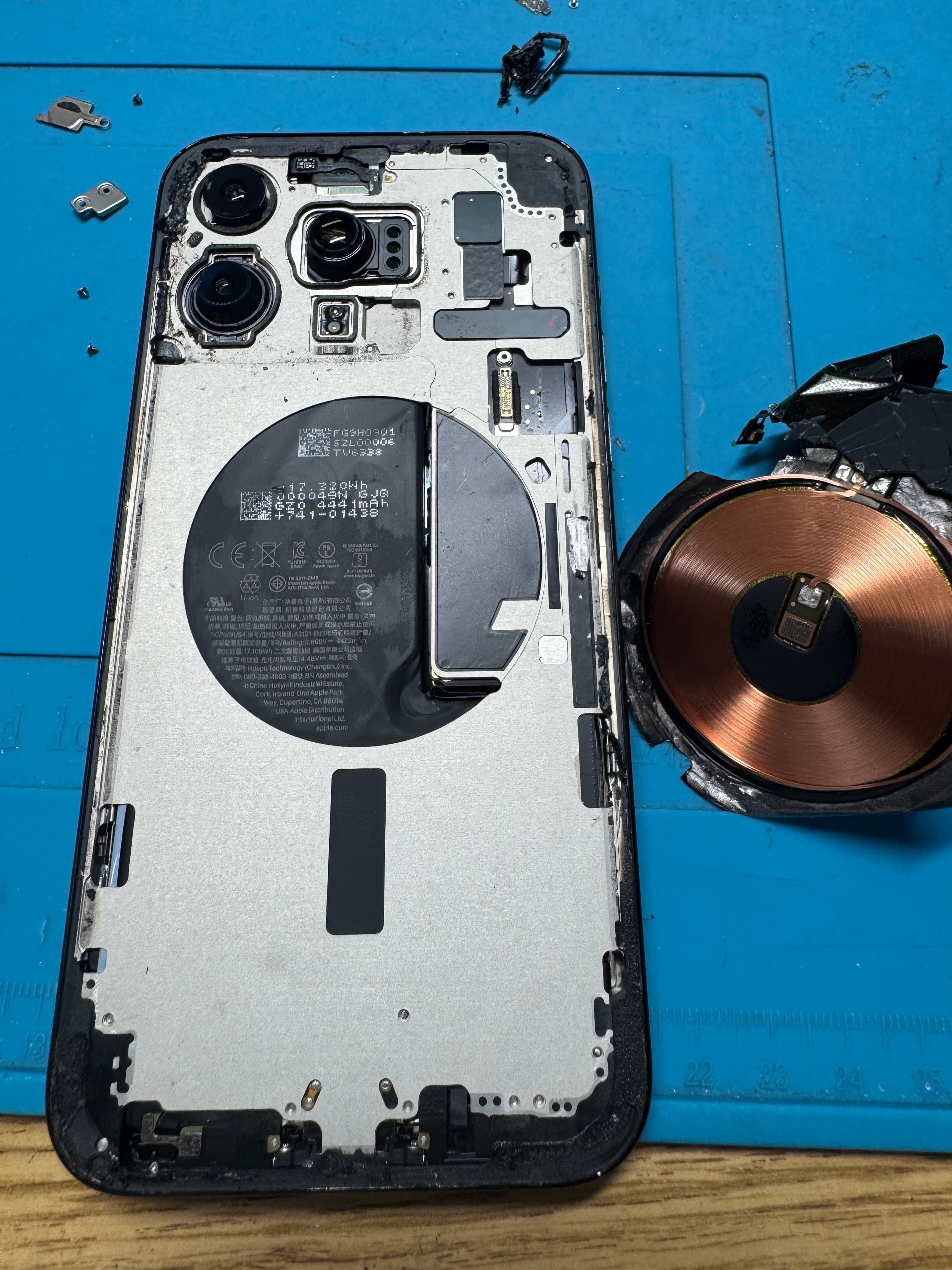 iPhone chassis on the KINGSELL bench with the wireless charging coil and broken back glass beside it